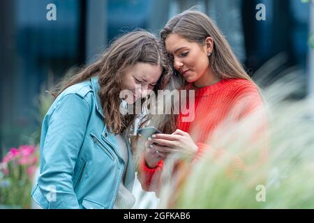 Zwei Freundinnen nutzen ein Smartphone, lachen und reden, Technologiekonzept mit immer verbundenen Milenials Stockfoto