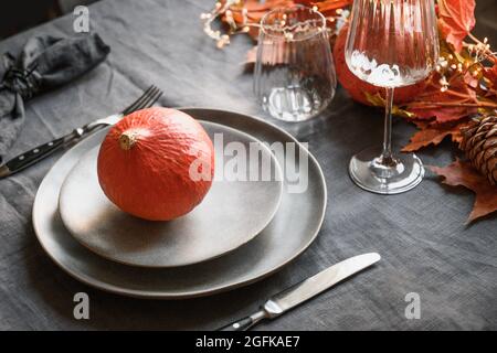 Thanksgiving-Tagestisch mit grauem, mit Kürbis verzierten Teller, gefallenen Blättern und Girlande auf einer grauen Tischdecke. Nahaufnahme. Frohe Halloween. Stockfoto