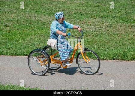 Eine farblich abgestimmte ältere Frau in einem Turban fährt ein alameda-Dreirad für Erwachsene im Kissena Park, Flushing, Queens, New York City. Stockfoto