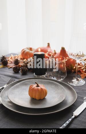 Thanksgiving-Tagestisch mit grauem, mit Kürbis verzierten Teller, gefallenen Blättern und Girlande auf einer grauen Tischdecke. Nahaufnahme. Frohe Halloween. Vertikal für Stockfoto