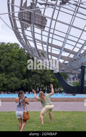 Ein Paar fotografiert im Flushing Meadows Corona Park in einer Pose, die den Anschein hat, als würde der Mann die Unisphere hochhalten. In Queens, New York. Stockfoto