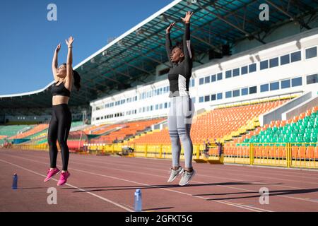 Verschiedene weibliche Athleten springen, während sie gemeinsam Burpee-Übungen im Stadion machen Stockfoto