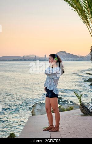 Junge asiatische Frau hört Musik mit dem Meer im Hintergrund Stockfoto