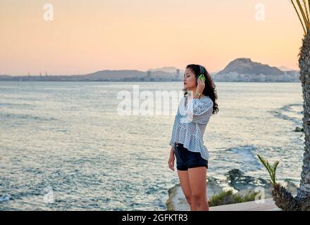 Junge asiatische Frau hört Musik mit dem Meer im Hintergrund Stockfoto