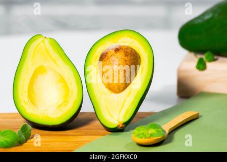 Hälften von reifen Avocado und Micro Green auf Holzbrett serviert auf dem Tisch, weißer Hintergrund, gesunde ölige Lebensmittel, Keto-Diät, Nahaufnahme. Stockfoto