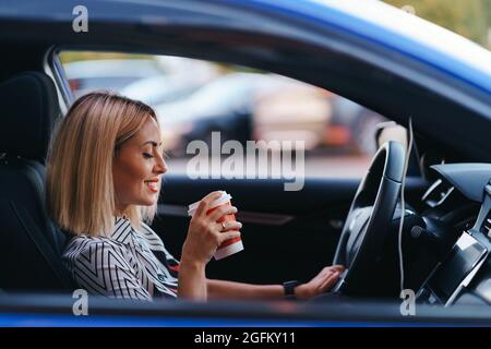 Moderne blonde Frau mit einem Kaffee zu gehen, während der Fahrt In der Stadt Stockfoto