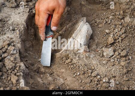 Archäologische Ausgrabungen, Archäologen arbeiten, graben ein altes Tonartefakt mit speziellen Werkzeugen im Boden Stockfoto