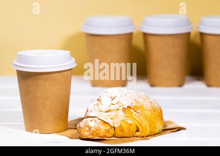 Kaffee zum Mitnehmen in einer Öko-Tasse aus Papier mit Mandelcroissant auf einem Holz- und hellorangenen Hintergrund, Fast Food, Copyspace, Koffeingetränk zum Mitnehmen Stockfoto