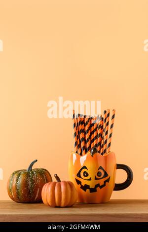 Halloween blank oder Einladung mit Party-Dekorationen, Bonbonschüssel, Kürbisse, Süßigkeiten, niedlichen Becher mit Trinkhalm auf orangefarbenem Hintergrund. Vertikale Kompos Stockfoto