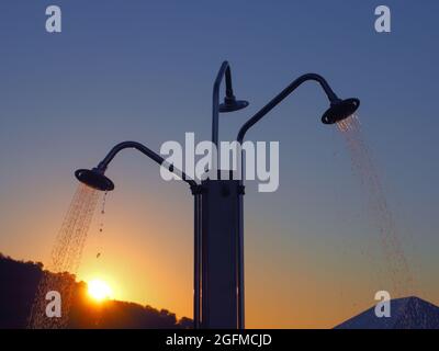 Dreifache Stranddusche mit fließenden Düsen aus zwei Gießkannen vor dem Hintergrund der untergehenden Sonne Stockfoto