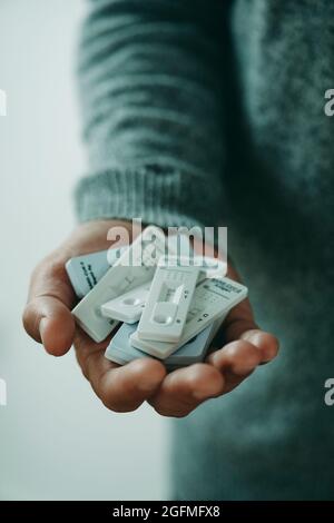 Ein junger Kaukasusmann, der einen grauen Pullover trägt, hat eine Reihe von Covid-19-Antigendiagnosetestgeräten in der Hand Stockfoto