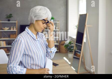 Müde stressige reife Geschäftsfrau, die an Augenmüdigkeit und Kopfschmerzen bei der Arbeit leidet. Stockfoto
