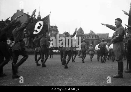 Hitler grüßt die Nazis, als er SA-Truppen (Brownshirts) zuschaut, die 1935 in Nürnberg vorbeimarschieren Stockfoto