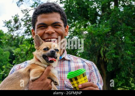 Afroamerikanischer Mann hält einen chihuahua Hund und trinkt Kaffee aus einer Einweg-Tasse Stockfoto