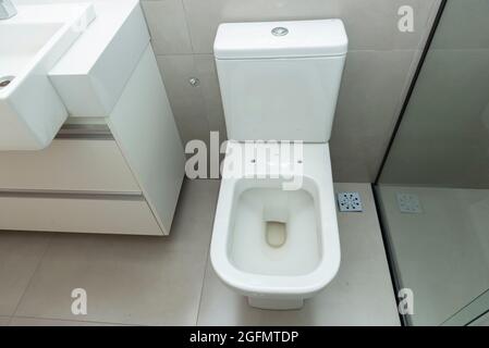 Blick von oben auf die saubere weiße Toilettenschüssel in einem modernen Badezimmer. Toilette ohne Deckel, um zwischen dem Waschbecken und der Dusche zu sitzen. Stockfoto