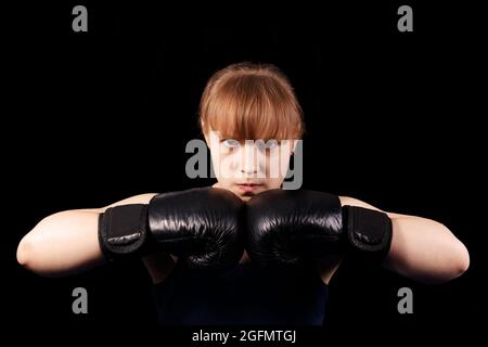 Porträt eines jungen Boxermädchen, das die Hände in schwarzen Boxhandschuhen vor schwarzem Hintergrund zusammenstellt Stockfoto