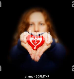 Das junge Mädchen hält in ihren Händen ein rotes Herz, umgeben von Dunkelheit Stockfoto