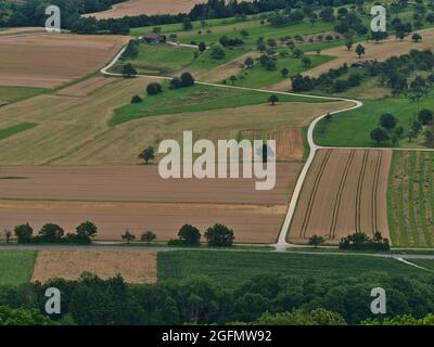 Luftaufnahme der Landstraße, die durch braune und grüne Felder mit Bäumen an den Ausläufern der Schwäbischen Alb bei Weilheim führt. Stockfoto