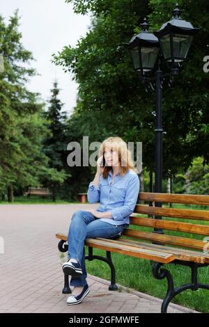 Allein eine junge Frau, die auf einer Bank sitzt und am Telefon spricht Stockfoto