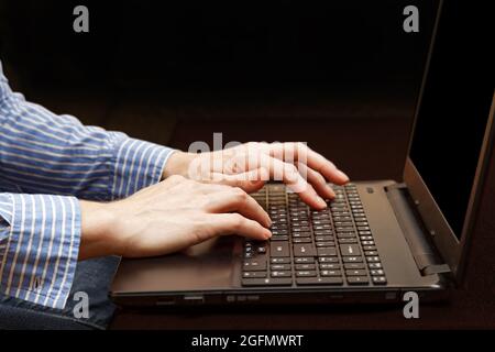 Menschliche Hand auf der Tastatur des Notebooks auf der Dunkelheit. Arbeiten am Computer, Schreiben eines Blogs, Suchen im Internet, Kommunikation in sozialen Netzwerken Stockfoto