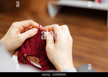 Nahaufnahme Womans Hände strickt rot burgunderrot Wollgarn mit Stricknadeln. Ansicht von oben. Geringer Fokus. Stockfoto