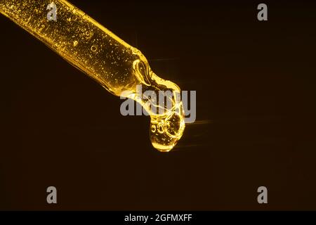 Ein Tropfen goldenes Serum aus einer Pipette mit Lichtern. Auf einem dunklen Hintergrund. Stockfoto