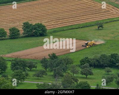 Luftaufnahme eines gelb gefärbten Erntearbeiters, der Getreide auf einem landwirtschaftlichen Feld erntet, das von Bäumen und Wiesen umgeben ist und von der Spitze des Limburger Hügels aus gesehen wird. Stockfoto