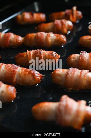 Kochen von Schweinen in Decken in einem elektrischen Gebläseofen . Schweine in Decken sind Würste oder Chipolatas, die in streifigen Speck eingewickelt sind und traditionell zu Weihnachten in Großbritannien gegessen werden. Es gibt Warnungen, dass es aufgrund von Problemen in der Lieferkette des Brexit einen Mangel an in Decken gekauften Schweinen im Supermarkt geben könnte Stockfoto