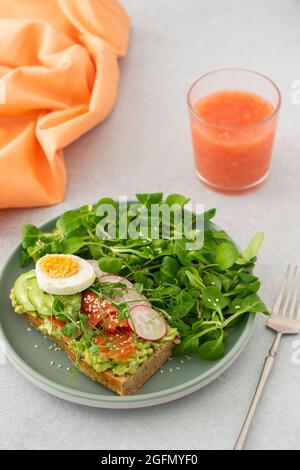 Gesundes, leckeres Frühstück, Sandwich mit Avocado und Lachs, Gurken und Radieschen sowie Mikrogemüse aus Erbsen mit gekochtem Ei und Maissalat Stockfoto