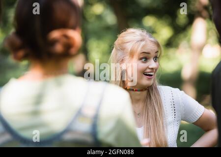 Aufgeregter Teenager, der in der Nähe verschwommener multiethnischer Freunde im Park steht Stockfoto