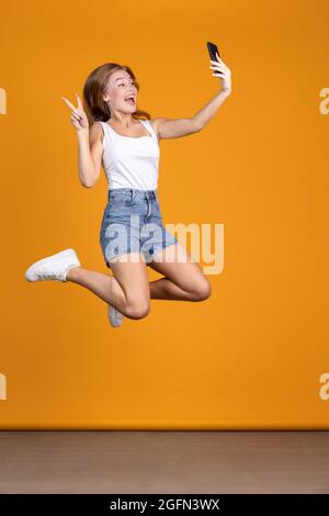 Ganzkörperfoto einer glücklichen, lächelnden und springenden Frau auf orangefarbenem Studiogelände Stockfoto