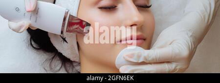Banner der hübschen jungen kaukasischen Dame während des Verfahrens der Reinigung der Haut mit Ultraschall-Scrubber. Ultraschallgerät in den Händen von Stockfoto