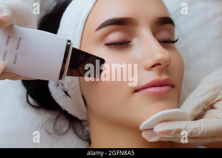 Nahaufnahme von oben Ansicht der hübschen jungen kaukasischen Dame während des Verfahrens der Reinigung der Haut mit Ultraschall-Scrubber. Ultraschallgerät in den Händen Stockfoto