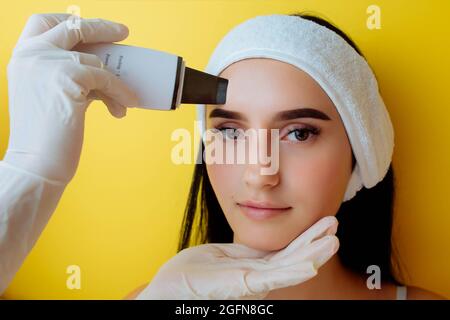 Nahaufnahme von oben Ansicht der hübschen jungen kaukasischen Dame während des Verfahrens der Reinigung der Haut mit Ultraschall-Scrubber. Ultraschallgerät in den Händen Stockfoto