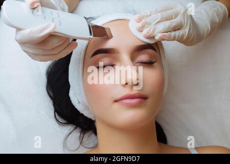 Nahaufnahme von oben Ansicht der hübschen jungen kaukasischen Dame während des Verfahrens der Reinigung der Haut mit Ultraschall-Scrubber. Ultraschallgerät in den Händen Stockfoto