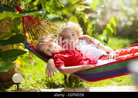 Kinder entspannen sich in einer bunten Regenbogenhängematte. Heißer Tag Garten Spaß im Freien. Junge spielt draußen. Brüder spielen draußen im sonnigen Hinterhof. Mittagsschlaf Stockfoto