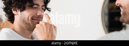 Fröhlicher und verschwommener Mann, der Creme auf die Nase des lächelnden Freundes, Banners auftrug Stockfoto