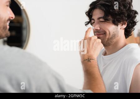 Fröhlicher und verschwommener Mann, der Creme auf die Nase des lächelnden Freundes applyte Stockfoto