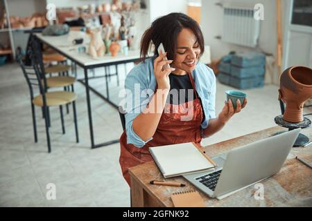 Fröhliche Frau, die in der Töpferwerkstatt telefoniert Stockfoto