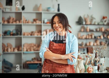 Fröhliche Keramikerin, die in der Töpferwerkstatt steht Stockfoto