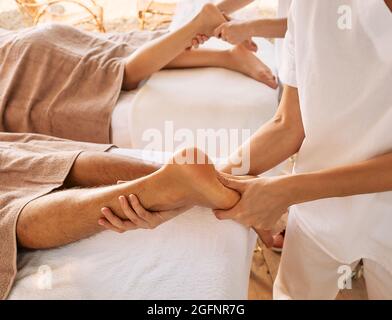 Fußreflexzonenmassage, Fußmassage aus nächster Nähe. Masseure drücken auf spezielle Fußpunkte für die Fußmassage eines Mannes und einer Frau in einem Spa-Salon Stockfoto