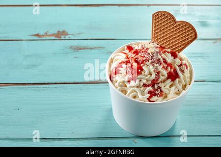 Cremige deutsche Vanille-Spaghetti Eis Sommer Dessert mit frischen Beeren Coulis gekrönt und serviert mit einem Wafer in einer Wanne in hohen Winkel über blauem Holz Stockfoto