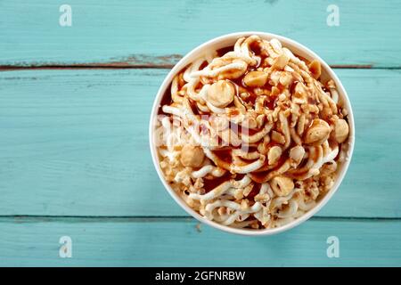 Köstliche trendige deutsche Vanille-Spaghetti-Eisbecher mit frischen Haselnüssen und Karamellsauce in einer Nahaufnahme von oben über blauem Holz wi gekrönt Stockfoto