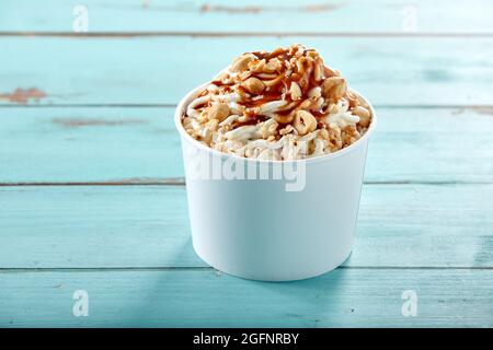 Köstliche Belag von Haselnüssen auf deutsche Vanille-Spaghetti-Eis beträufelt mit Karamellsauce und serviert in einer Wanne in einer Seitenansicht über blauem Holz Witz Stockfoto