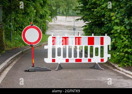 Barrieren auf einer Straße mit Barrikade und kein Durchgangsschild. Die Straße ist aufgrund der Flutflutung im Hintergrund nicht befahrbar. Stockfoto