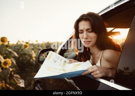 Verlorene junge Frau, die in ihrem Auto auf dem Land sitzt und auf die Karte schaut Stockfoto