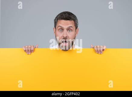 Überrascht reifer bärtiger Mann hinter gelbem Papier mit Textbild, Werbung Stockfoto