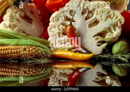 Verschiedene frische Gemüse auf einem schwarzen reflektierenden Hintergrund. Tomaten, Paprika, Blumenkohl, Chili, Gurken, Mais und Rosmarin werden präsentiert. Stockfoto
