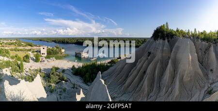 Rummu, Estland - 12. August 2021: Kalksteinberge und ruhiger blauer Grundwassersee in einem alten Steinbruch mit verlassenen Gebäuden im Wasser Stockfoto