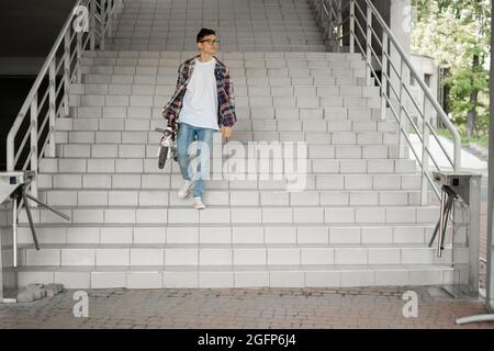 Ein Student steigt mit einem Elektroroller die Treppe zur Universität hinab. Modernes Stadtkonzept. Ökologischer technologischer Lebensstil. Stockfoto